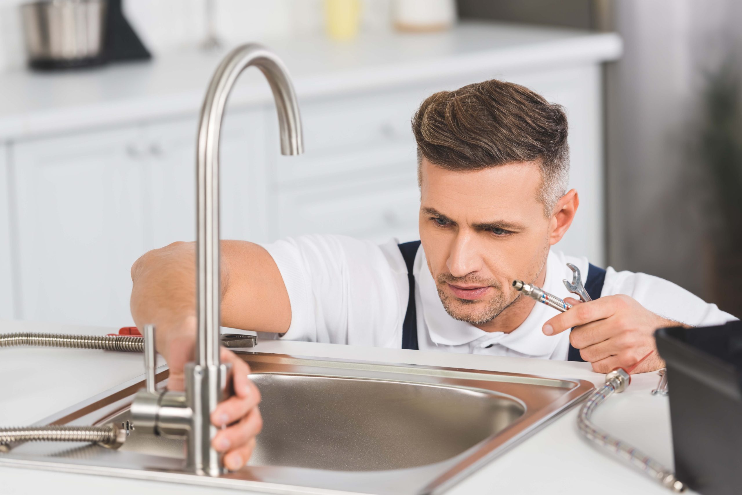 adult repairman holding pipe and spanner while repairing faucet