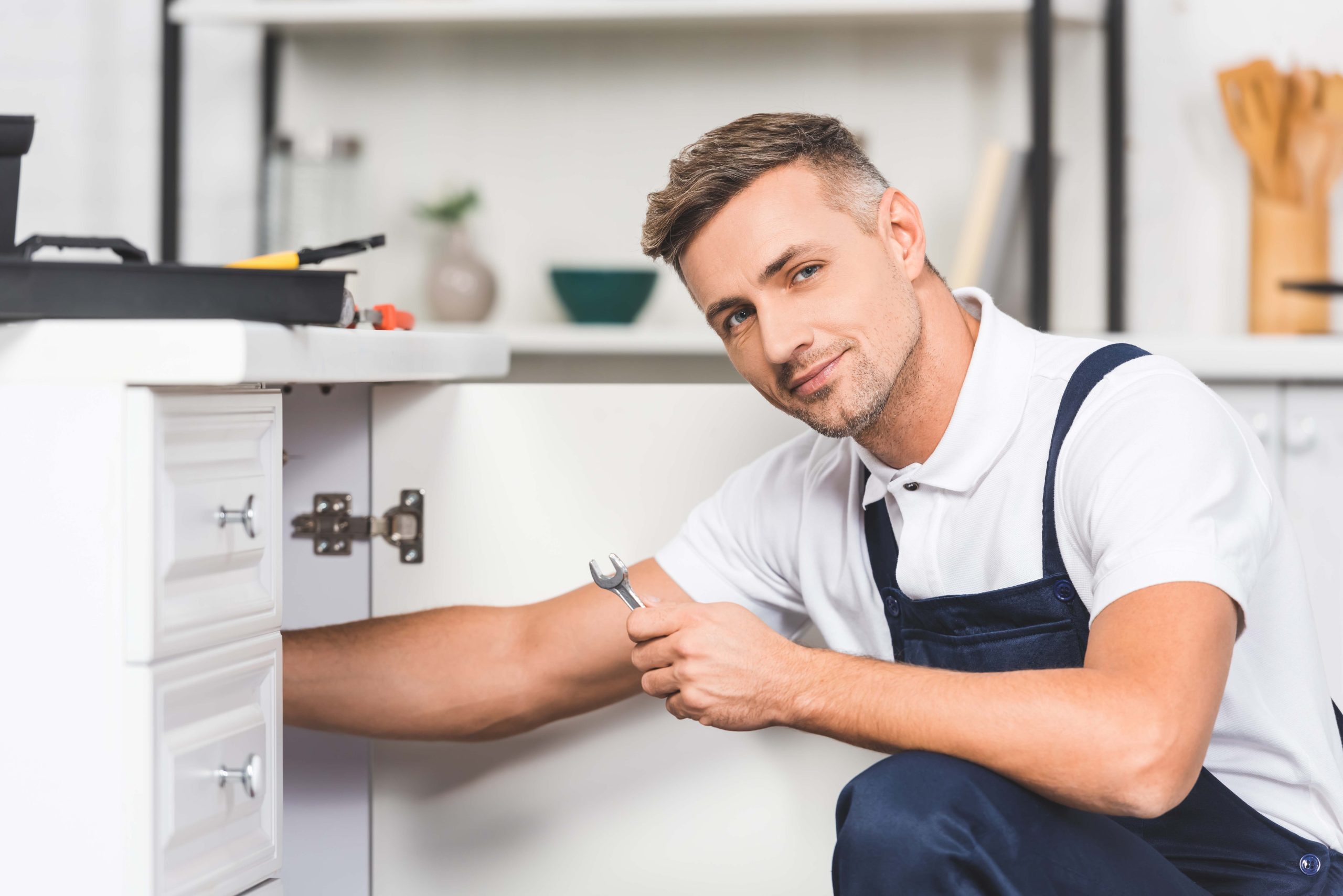 adult repairman repairing pipes of sink by spanner at kitchen an